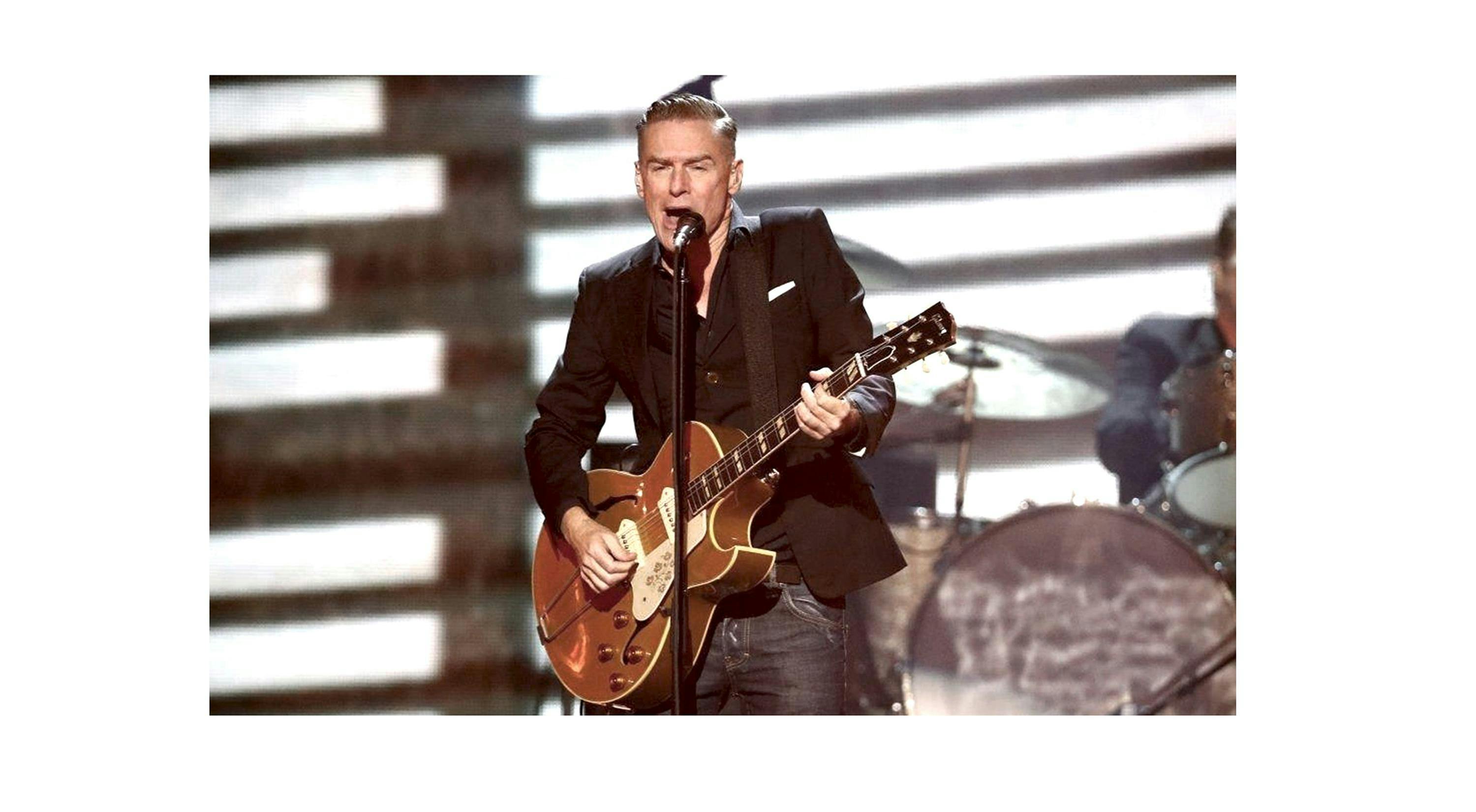 Der Sänger Bryan Adams, steht mit der Gittare in der Hand auf einer Bühne vor eine Mikrofon. © _┬®©Reuters_Bryan_Adams